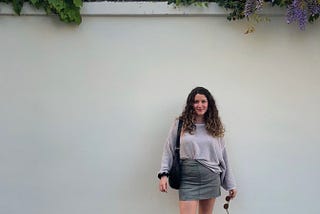 Woman stands in front of blank wall, flowers spill over the top of the wall