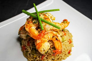 A plate of fried rice garnished with two large shrimps and chives.