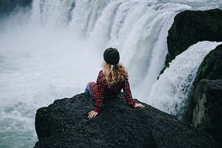 A woman sitting on edge of cliff on waterfall.