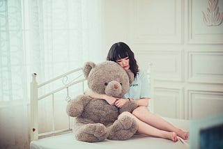 Woman Hugging Gray Bear Plush Toy on White Mattress