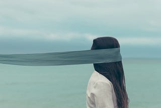 Abstract photo of a woman who can’t see because her eyes are covered by a piece of cloth.