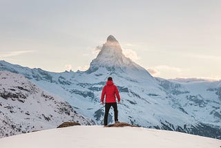 A man on a slope staring up at a mountain peak in the near distance.