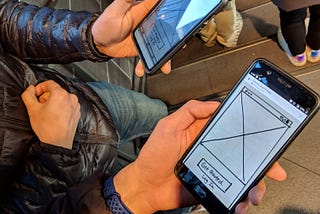 Two people holding up their phones and showing a prototype on their phone screens.