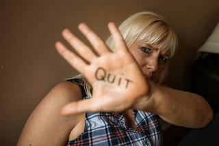 A woman with her hand up and quit written on her palm.