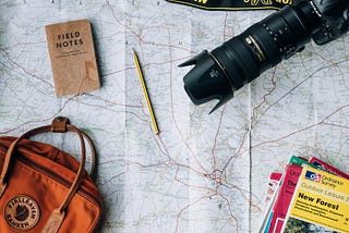 A picture of a travelling kit, including backpack, camera, guidebooks, feild notes, a pencil and a map.