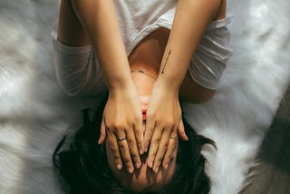 Girl lying on a white background covers her face with her hands