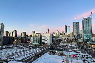 Photo of Calgary city skyline at sunset. Skyscrapers sit underneath a pinky blue sky