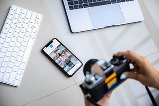 Photographer taking a picture of a keyboard, laptop, and smart phone.