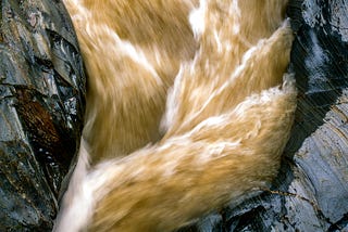 Yellow colored water passing by a gorge of black rocks.