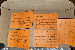 A paper box cap with 5 orange post-its that have a slightly different layout and handwriting. They al write: “Hey Vlad! Congratulations for winning Miro 2024 Pull Request Awards! — Alex P.”