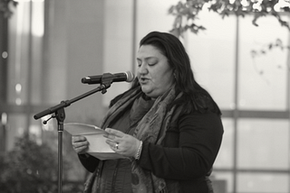 Woman in front of microphone reading from a piece of paper