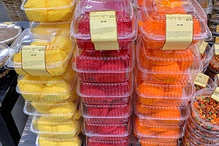 A picture showing stacks of plastic clamshell containers filled with brightly colored cake frosting. Image by Author.