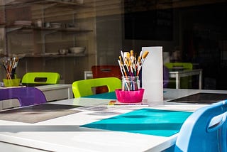 Paintbrushes and paper on a classroom table. Photograph courtesy of Charisse Kenion on Unsplash.