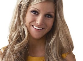 Head shot of Nikki Grahame with her long blonde hair down smiling at the camera. She is wearing yellow.