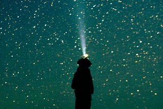 A person shining a flashlight up into the starry sky