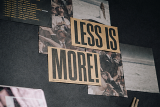 Image of a wall with images, text stuck to it with two big paper cards that read “Less is more”.