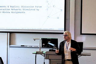 Daniel Braconnier speaks in front of a podium; a slide with text displays in the background.