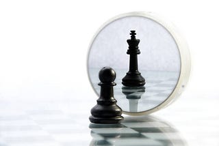 Pawn looking through the magnifying glass and seeing itself as King piece. image from Istock photos