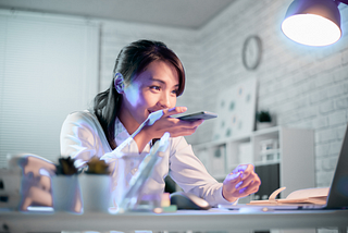 A woman sits at her desk reading her laptop while talking on her phone