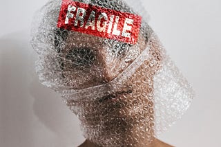 Person with bubble wrap on their head with a red sticker and the word Fragile in white text