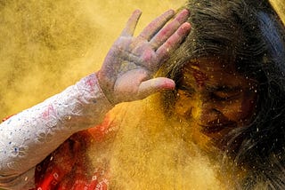 Indian girl holds up hand, being hit with powder