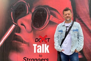 The author Stefan Thomas in front of a banner with the words Talk to Strangers behind him.