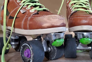 Up close photo of my ruffed up, scuffed up roller skates. Tan boot with a black stripe on the side. Neon green laces. Light green toe stops and black wheels covered in dirt.