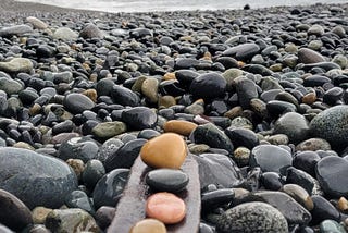 pebbles of different color held on a piece of wood overlooking the ocean
