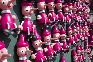 Numerous Pinocchio minifigures with long noses hanging on a wall.