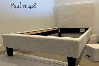 A white bed frame under construction. The words from Psalm 4:8 (In peace I will lie down and sleep: for you alone, Lord, make me dwell in safety) are overlaid at the top of the image.