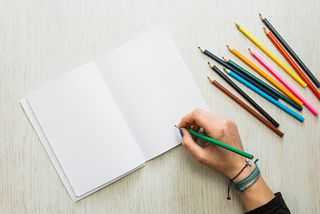 Image of a woman ready to write in a blank notebook with a green colored pencil.