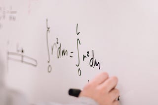 hand writing a mathematical equation on a white board