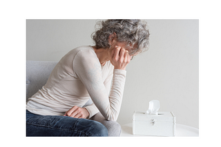 Gray haired woman hunched over a box of tissues