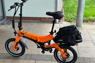 An orange e-bike, MiRiDER brand, with a bike bag on the back rack.