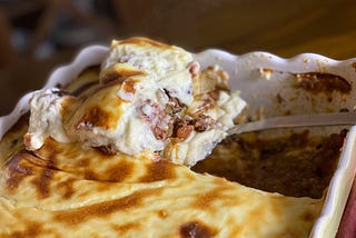 A slice of moussaka is lifted out of its baking dish.