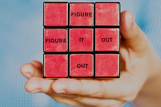 Person holding a solved rubik’s cube with the words “figure it out”.