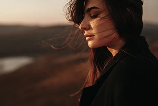 A woman stands alone by a lake.
