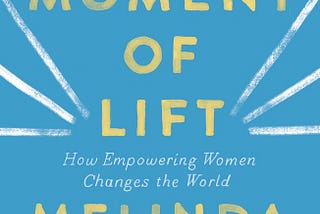 A photo of a book called The Moment of Lift: How Empowering Women Changes the World by Melinda Gates. The cover has a blue background with yellow and white writing and three white streaks on each side of word lift.