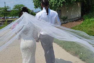 Backs of bride and groom walking hand in hand at Detroit River Walk