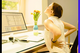 a woman sitting at the desk with both hands behind her back in pain