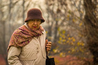 An older woman bundled up for an autumn walk in the forest.