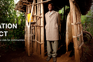 Picture of a person standing in front of a rural setting in front of a bamboo-made bathroom structure, the man is looking upward and smiling positively.