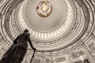 A picture of the U.S. Capitol Building Rotunda, at an angle from the ground up, including the bronze statue of George Washington positioned near the south door of the Rotunda.
