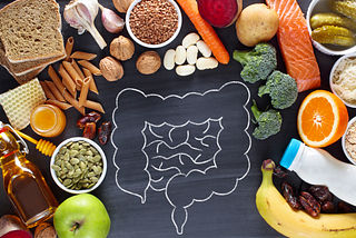 A picture of a colon drawn in chalk surrounded by fruits, vegetables, nuts, seeds and other foods indicative of gut health.