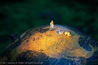 Two women are in the spotlight, cleaning and caring for North America on a desktop globe. Work at Hand by Audrey A. Heller