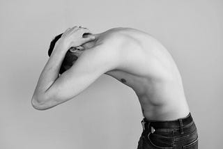 Shirtless man bending with his hands on his neck.