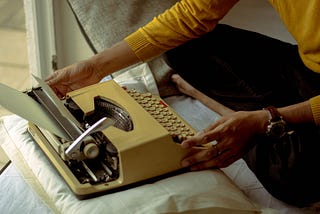 Someone wearing a yellow sweater using a type writer on top of a pillow