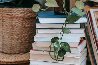 A stack of books with a plant perched on top, its fronds furling down onto the books.