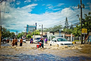 People navigating knee-high water in a flooded city street