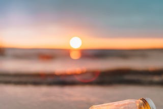 A beach scene at sunset. A glass jar sits on its side. Enclosed are a string of fairy lights.